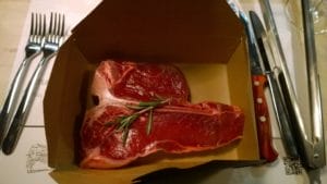 A paper box with a steak and a knife and fork