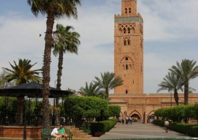 A large clock tower next to a palm tree with Koutoubia Mosque in the background