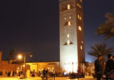 A clock tower lit up at night with Koutoubia Mosque in the background