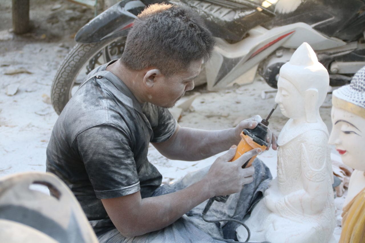 Künstler bearbeitet das Gesicht einer Buddhastatue Mann mit Schleißgerät und weiße Buddhafigur