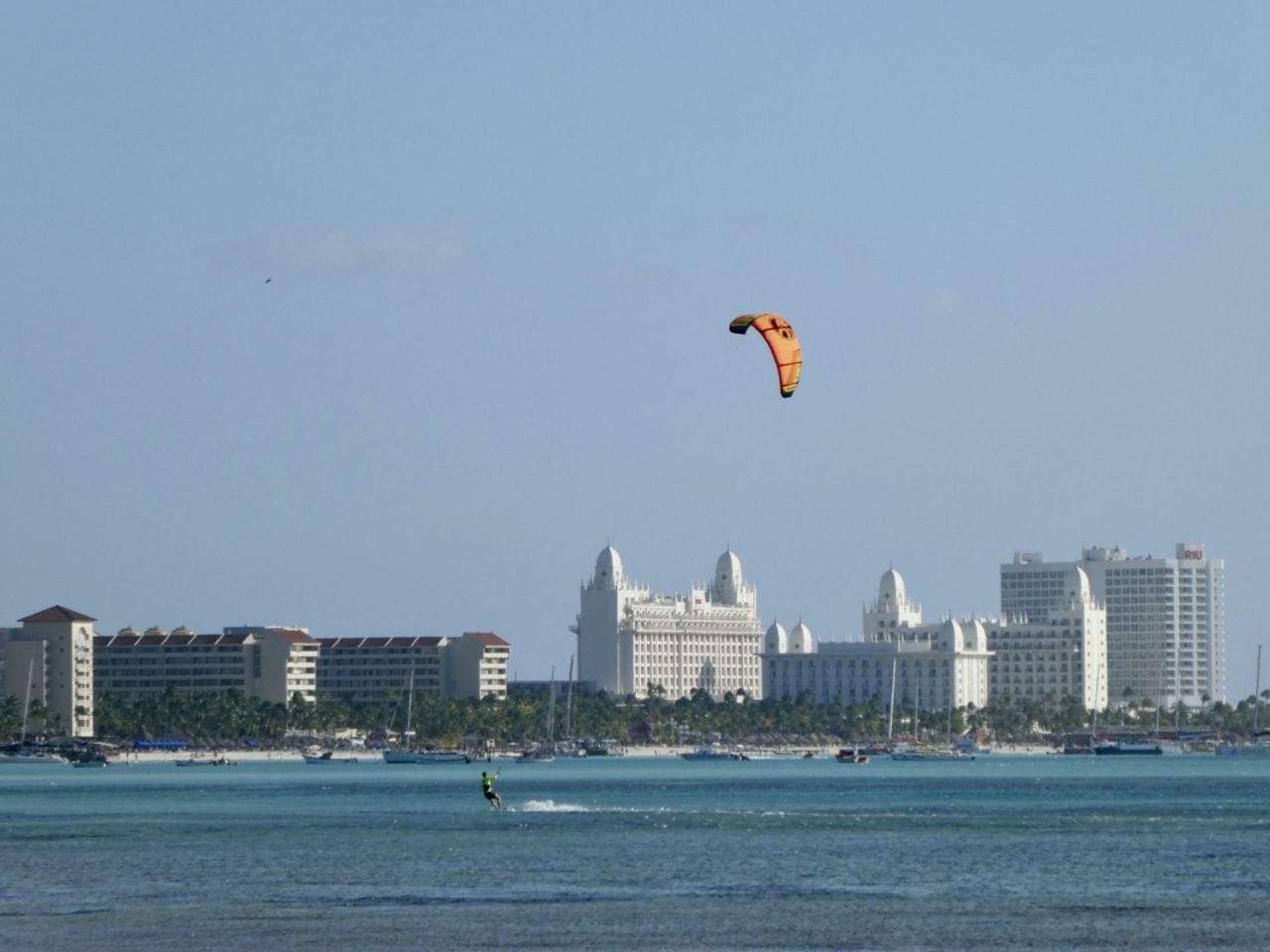 Ein Kitesurfer im Meer mit blauem Himmel und Hotels im Hintergrund