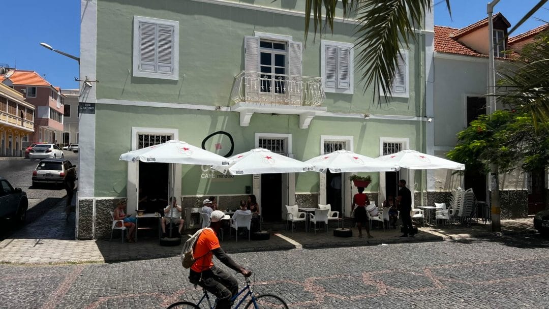 Grünes Cafe mit Schirmen und Fahrradfahrer im Vordergrund