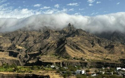 Eine von Wolken bedeckte Bergkette mit einem Dorf im Hintergrund.