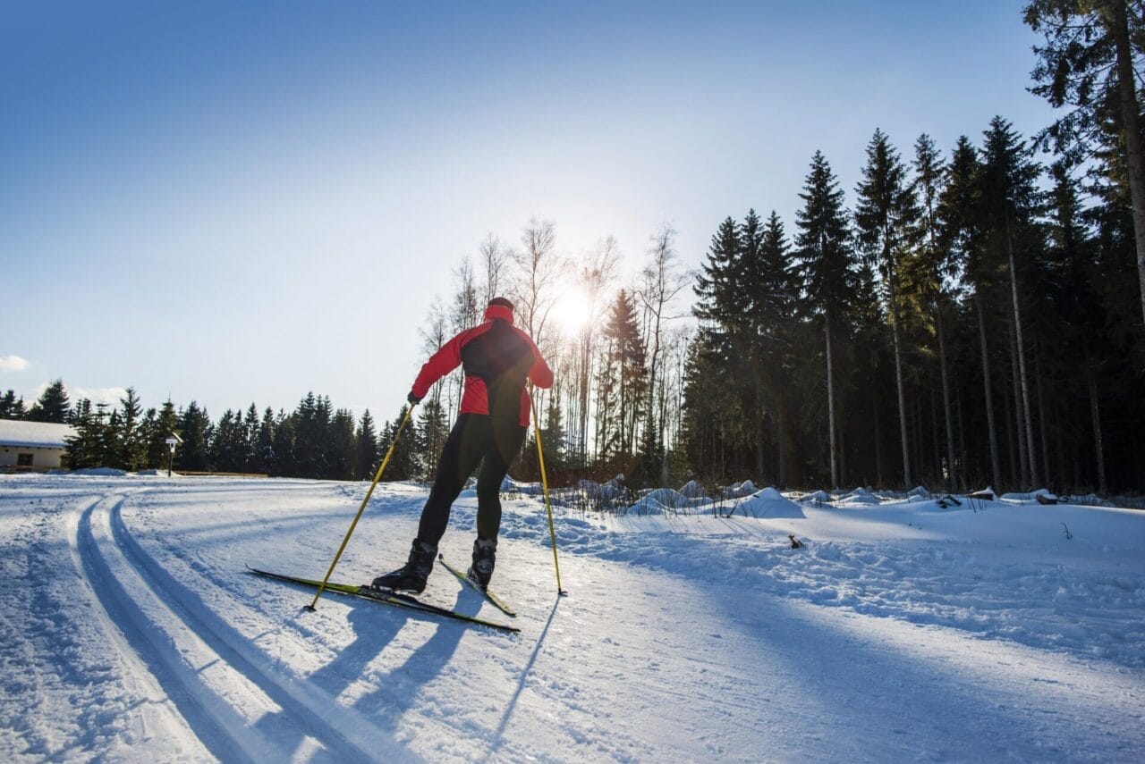 Ein Mann auf Skiern überquert einen verschneiten Weg.