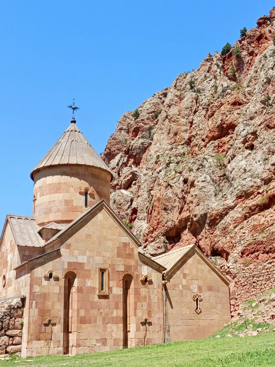 kloster-norawak Eine kleine Steinkirche mit einer konischen Kuppel steht vor steilen, felsigen roten Klippen unter einem klaren blauen Himmel.